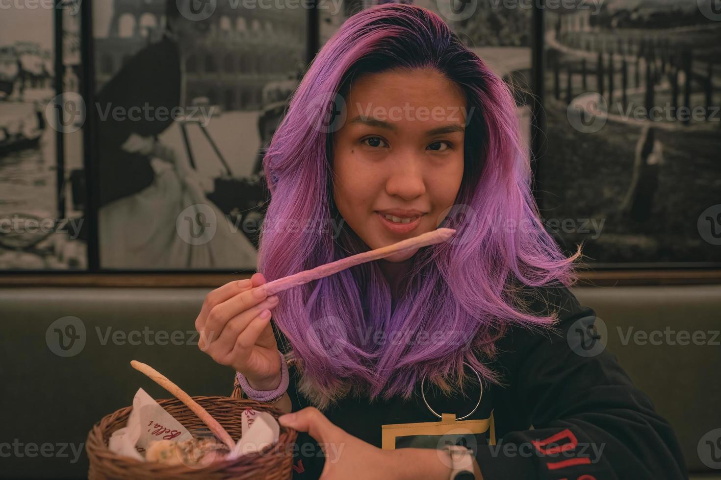 Purper haar- Aziatisch vrouw aan het eten een broodstengel Bij de Italiaans restaurant foto