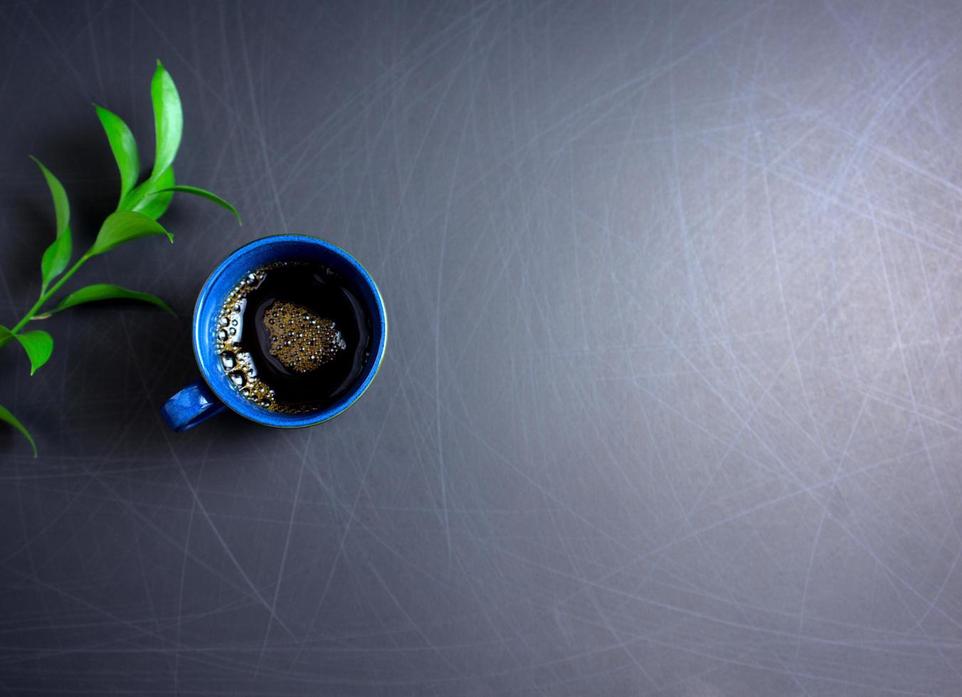 zwarte koffie met gouden schuim en groen blad plat lag op gekraste achtergrond foto