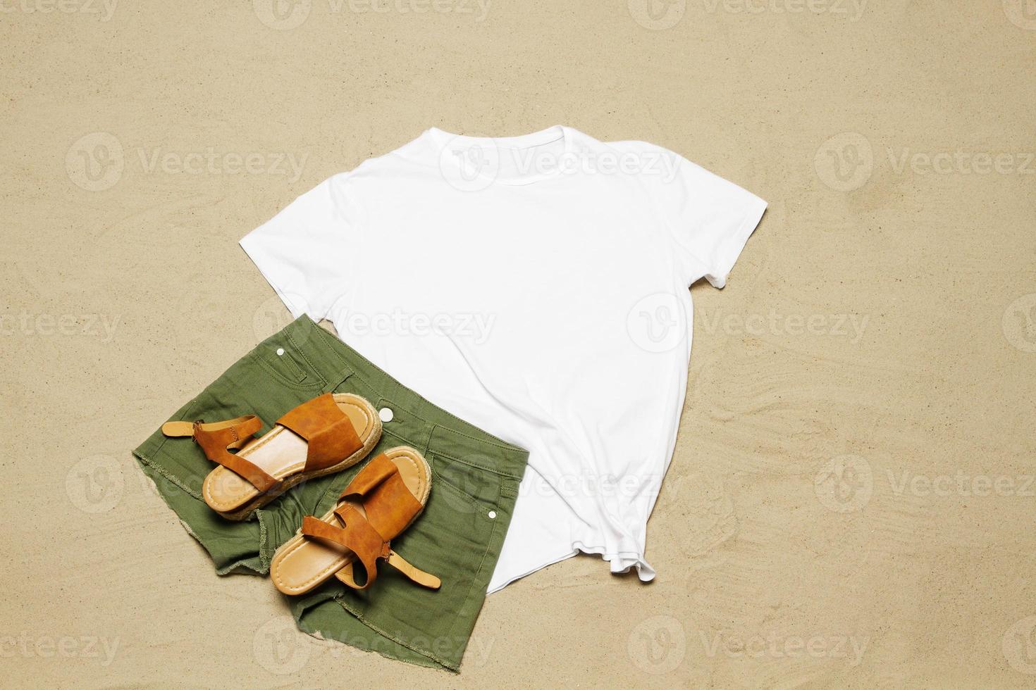 zand strand structuur achtergrond. mockup wit zomer t-shirt kopiëren ruimte. blanco sjabloon vrouw overhemd top visie. zomertijd accessoires jeans, sandalen. plat leggen detailopname t-shirt kust. strand tijd foto