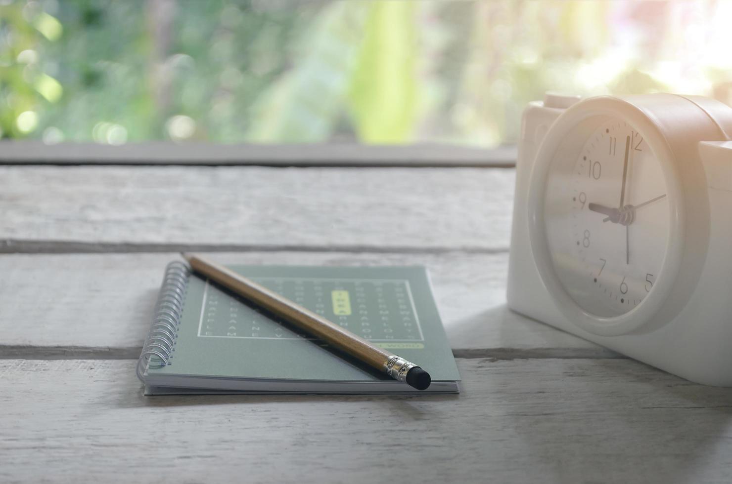 groen boek, potlood en wekker op een witte houten tafel foto