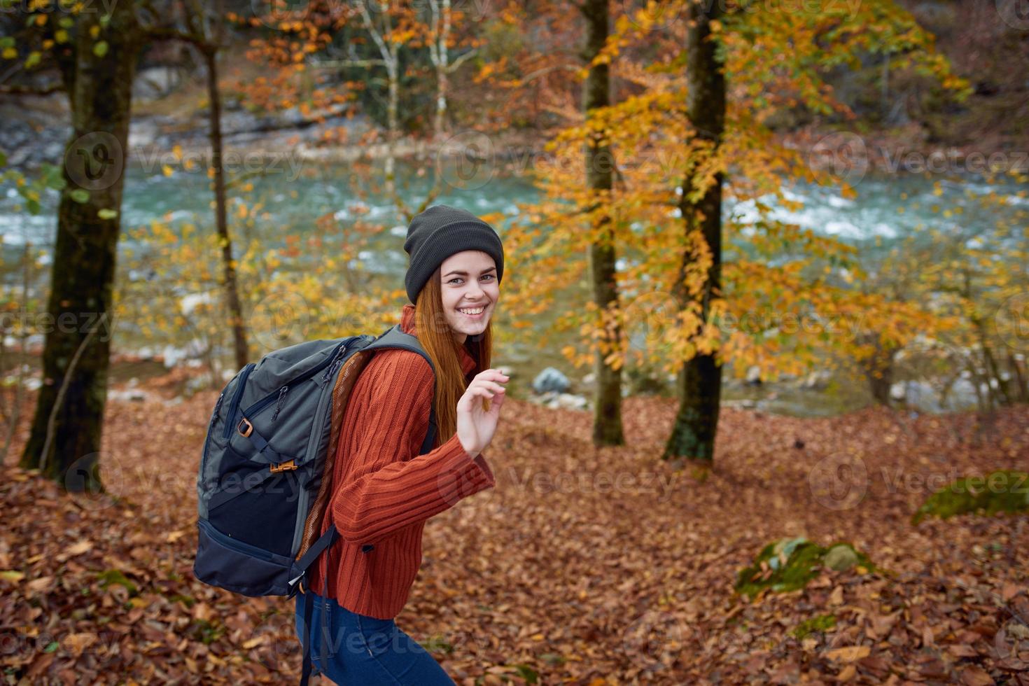 vrouw in een trui met een rugzak Aan haar terug in de buurt de rivier- in de bergen en park bomen herfst landschap foto