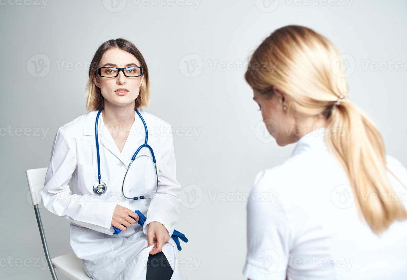 dokter zit Aan een stoel en een vrouw geduldig binnenshuis Aan een licht achtergrond foto