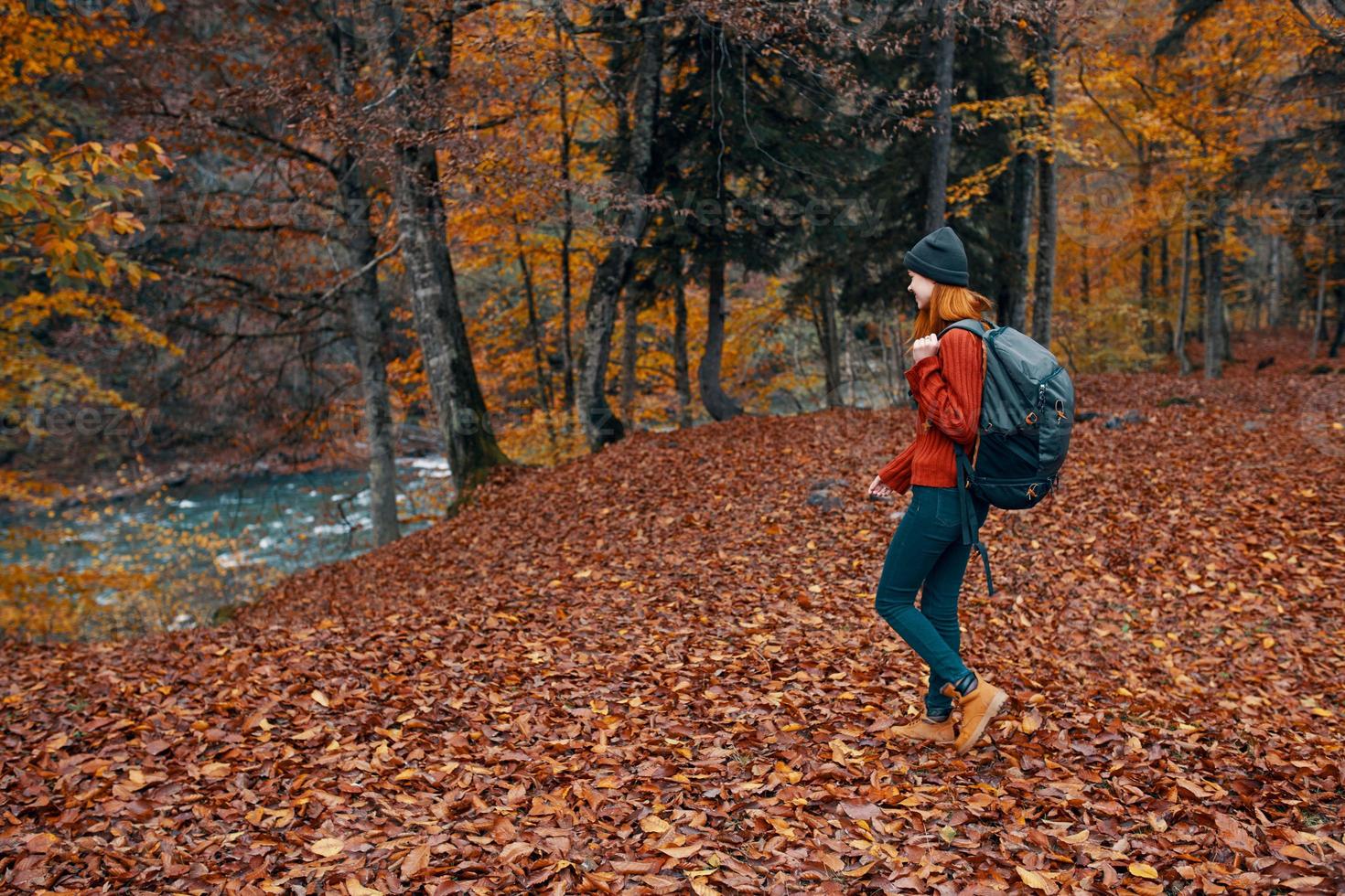 vrouw in herfst in de park met gedaald bladeren en een rugzak Aan haar terug rivier- in de achtergrond foto