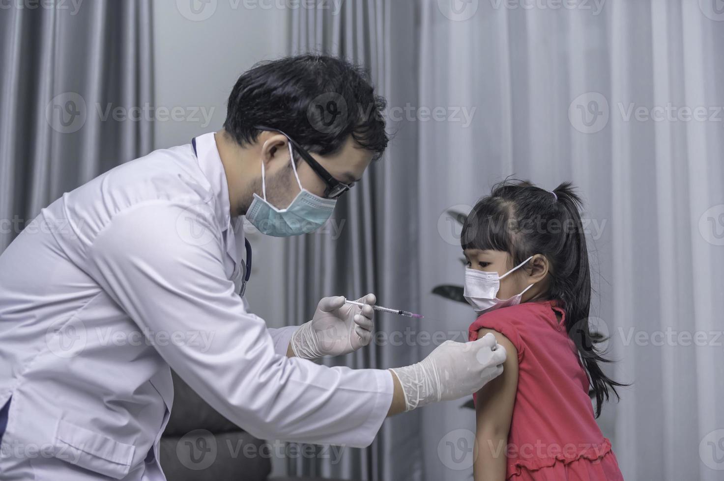 Aziatisch dokter injectie vaccin voor beschermen virus covid-19 naar een meisje slijtage medisch masker, mensen zijn meisjes zijn gevaccineerd tegen influenza elke jaar. foto