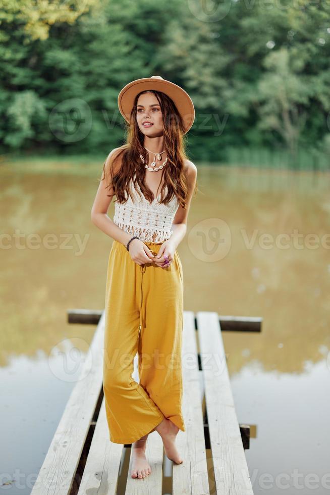 een jong vrouw in een hippie kijken en eco kleding reist buitenshuis door de meer vervelend een hoed en geel broek in de vallen foto
