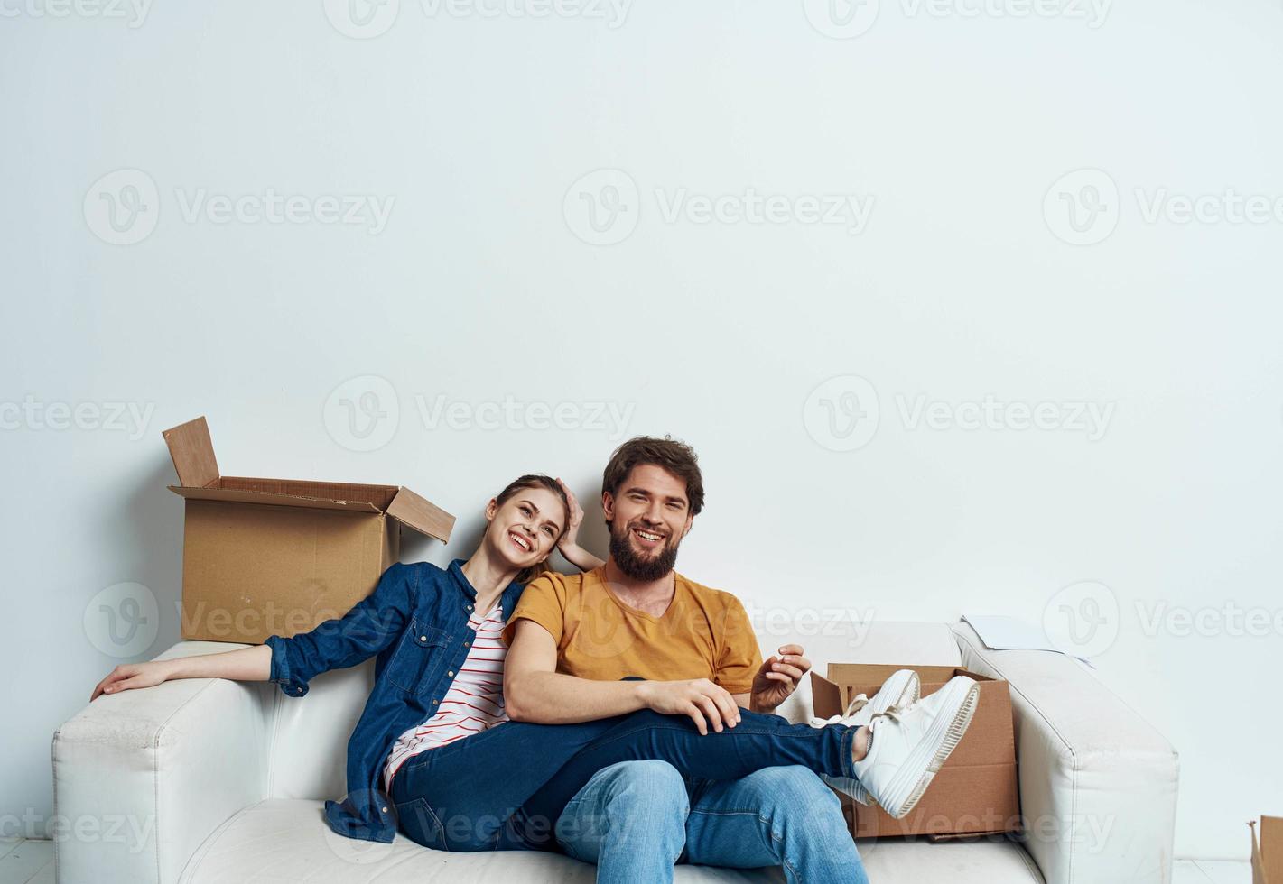 Mens en vrouw zitten Aan wit bankstel dozen met in beweging levensstijl dingen foto