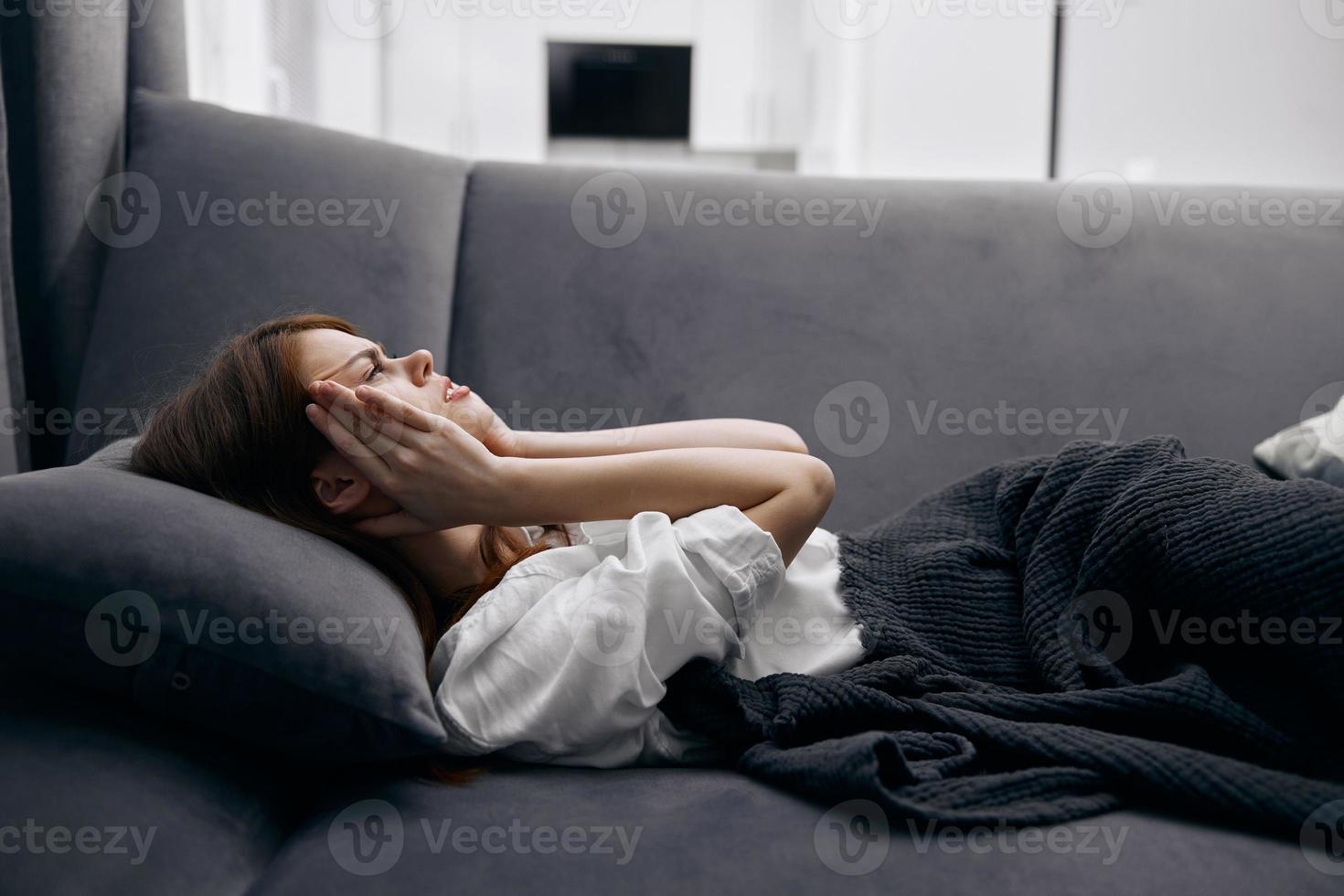 vrouw in de leven kamer aan het liegen Aan de bankstel handen Aan gezicht gevoel onwel foto