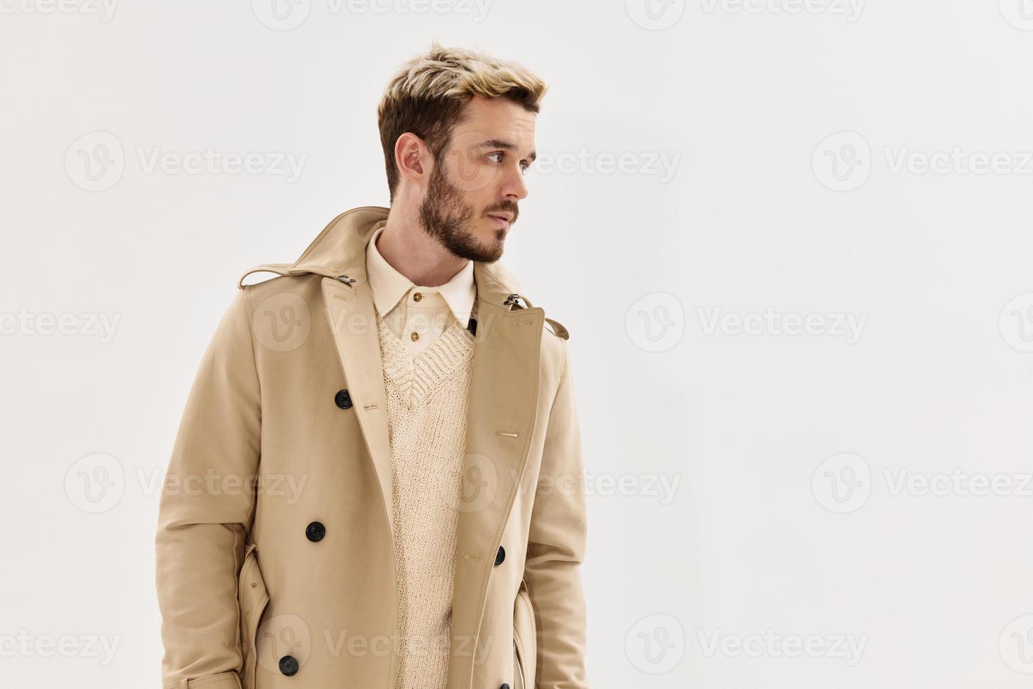 knap Mens in beige jas modieus kapsel kant oogopslag licht achtergrond foto
