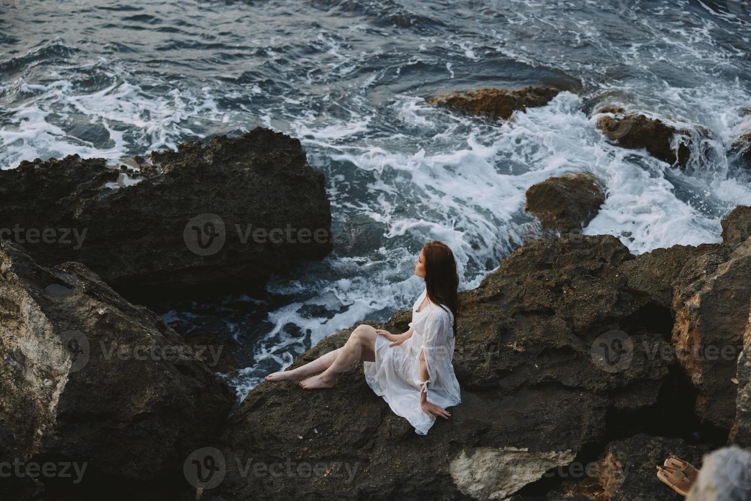 blootsvoets vrouw in een bruiloft jurk Aan de klif golven bewolkt weer foto