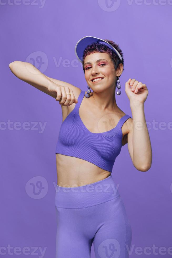 sport- mode vrouw dansen poseren glimlachen met tanden in een Purper sport- pak voor yoga Aan een slank lichaam en een transparant pet Aan haar hoofd Aan een Purper achtergrond monochroom foto