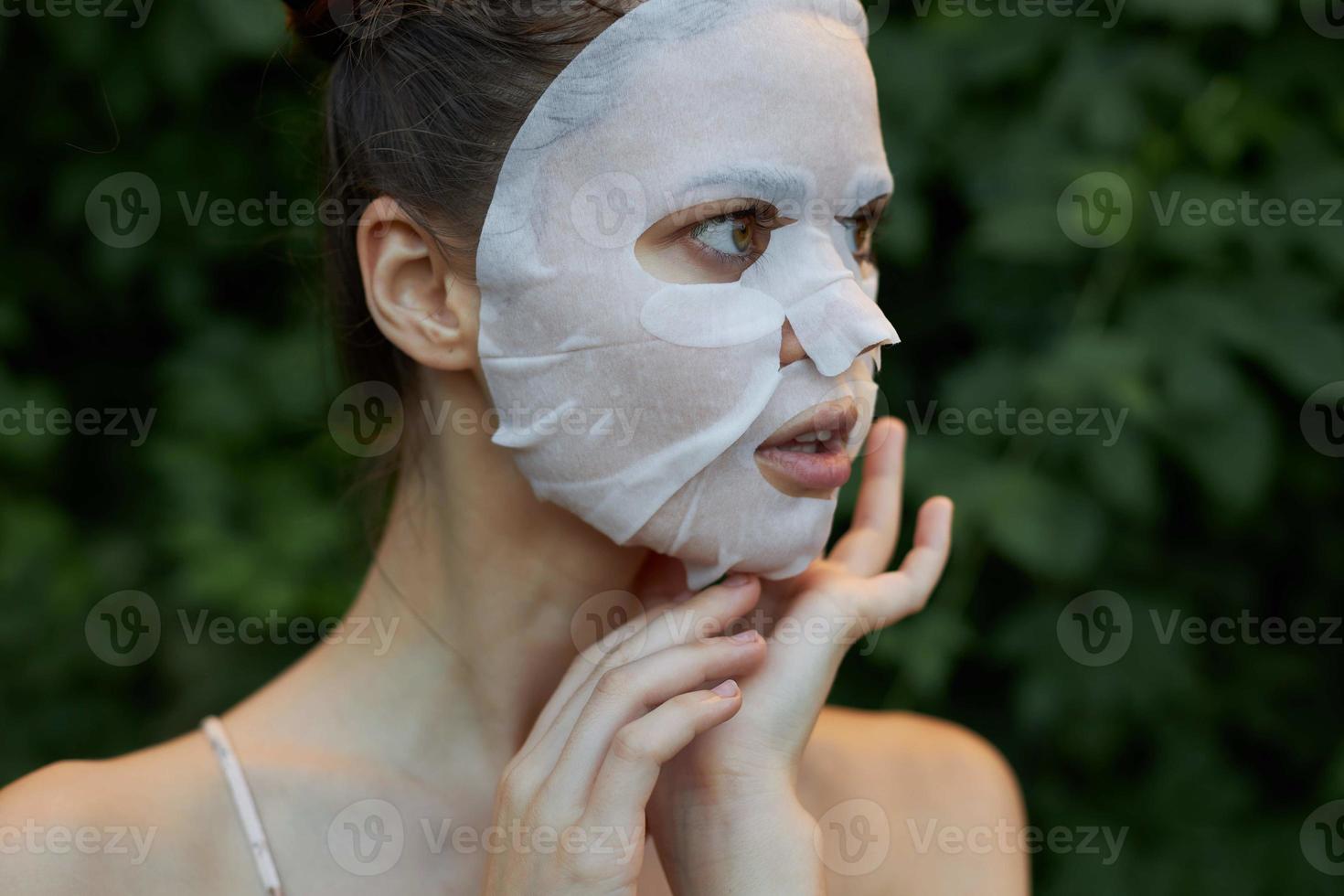 mooi hoor vrouw houdt zijn hand- in de buurt zijn gezicht wit masker huid zorg bladeren in de achtergrond foto