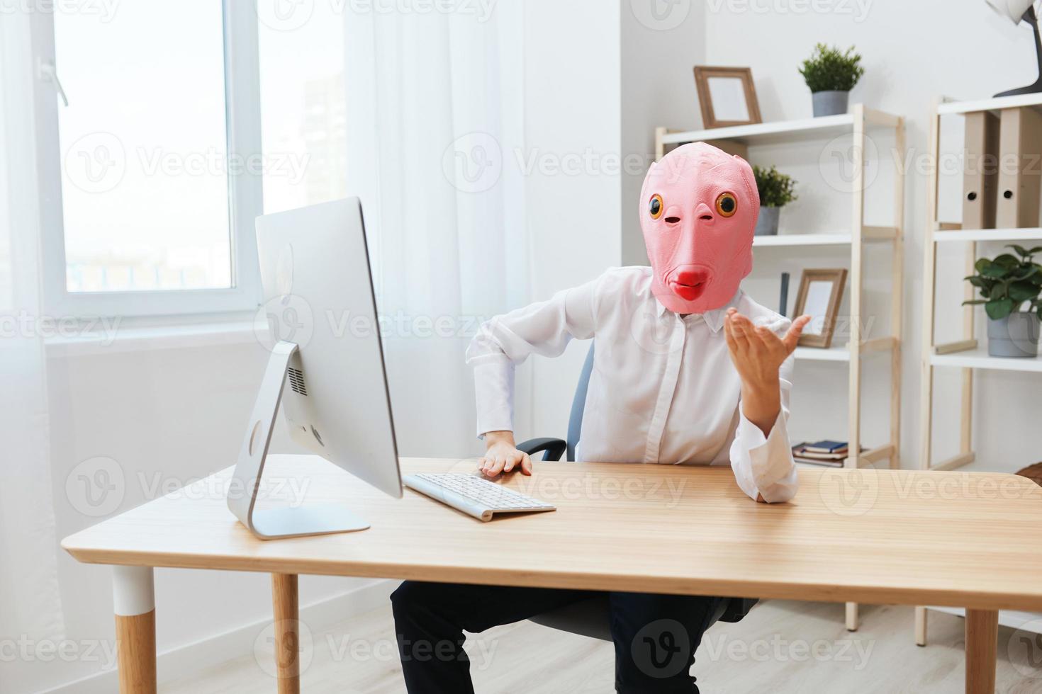 grappig gek zakenvrouw arbeider freelancer in roze vis masker werk Aan computer online nadenken of maken besluit geschokt door operationeel problemen verhogen hand- omhoog in licht modern kantoor. kopiëren ruimte foto