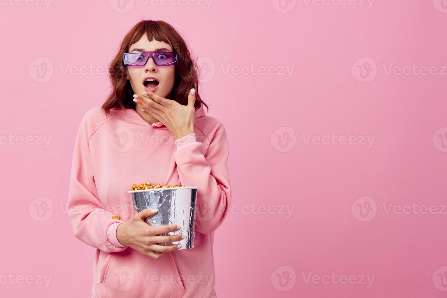 opgewonden dolblij gelukkig schattig roodharige dame in roze capuchon zonnebril met popcorn poseren geïsoleerd Aan over- roze studio achtergrond tonen kopiëren ruimte spandoek. mode bioscoop concept. vermaak aanbod foto