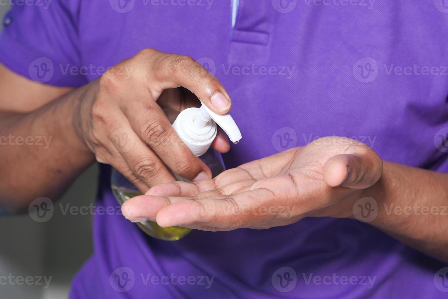 man in paars shirt met handdesinfecterend middel foto