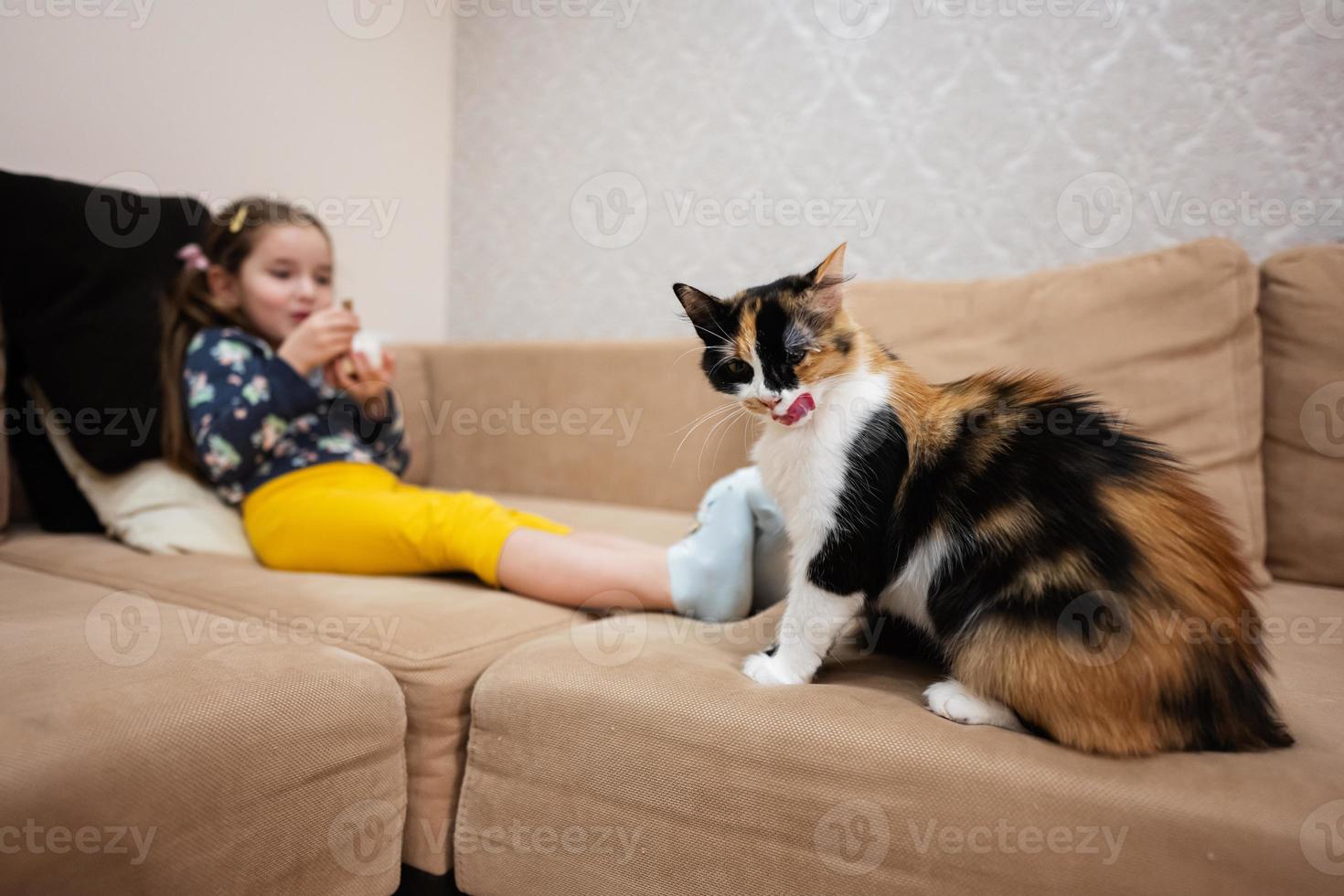 weinig meisje voeden de kat met yoghurt van een lepel Bij huis. foto