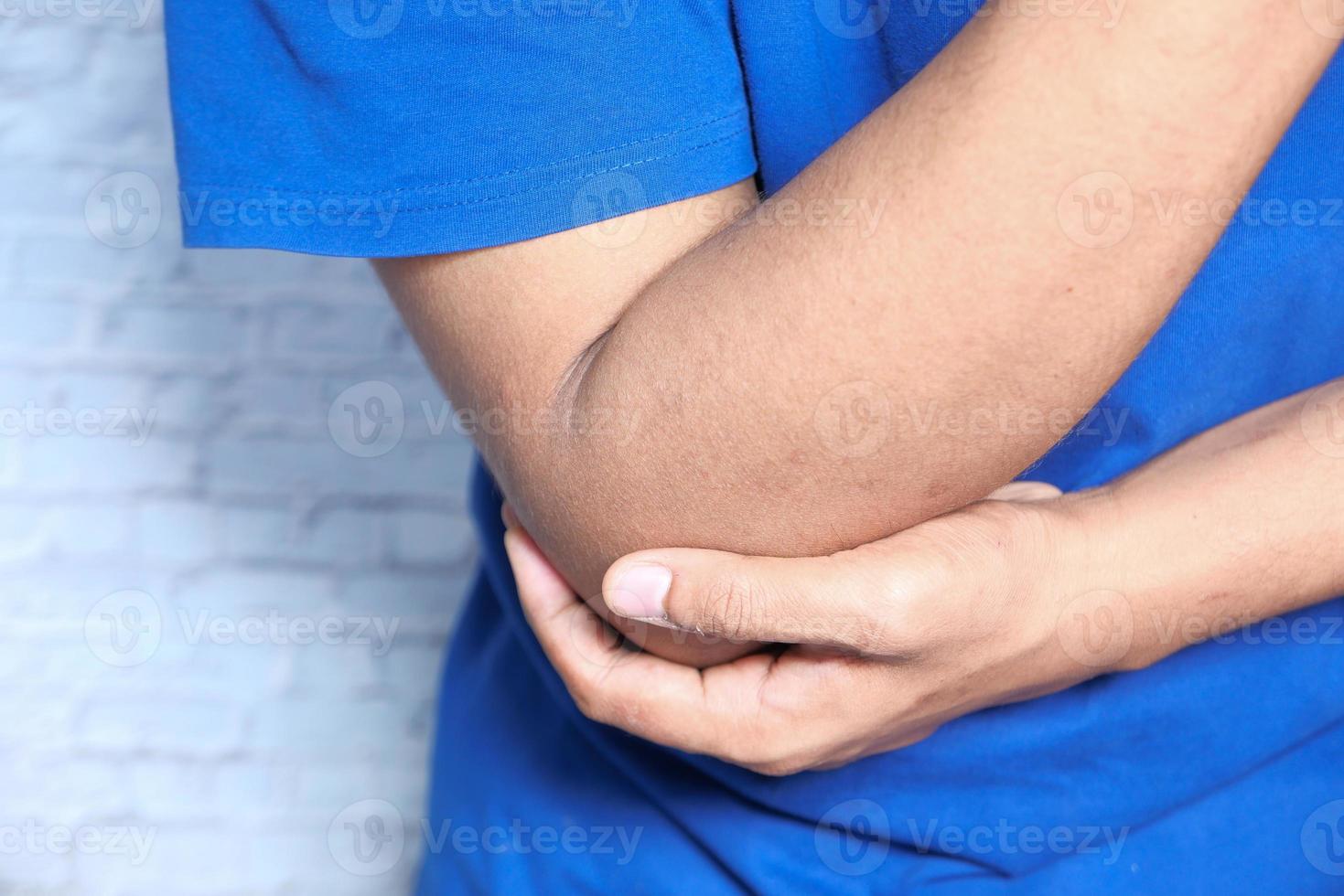 man in blauw shirt met elleboog pijn foto