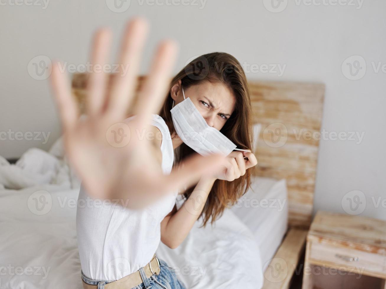 prikkelbaar vrouw covers haarzelf met haar handen van de camera en zit Aan de bed binnenshuis foto