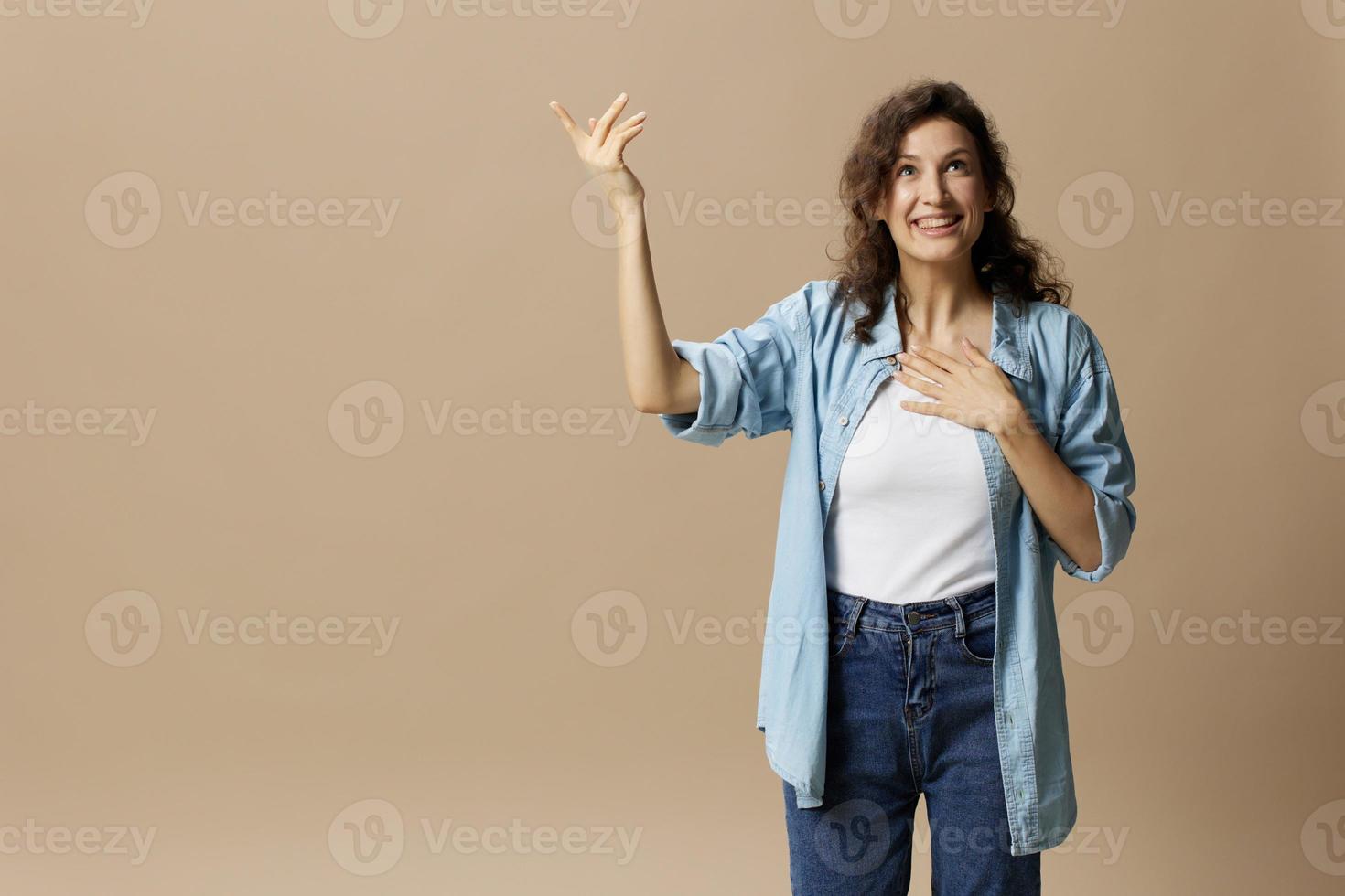 opgewonden gelukkig genoten gekruld mooi vrouw in jeans gewoontjes overhemd punt handen looks omhoog Bij vrij plaats poseren geïsoleerd Aan over- beige pastel achtergrond. mensen levensstijl emoties concept. kopiëren ruimte foto