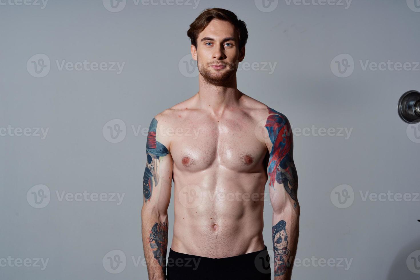 sportief Mens met een naakt torso gemotiveerd omhoog druk op tatoeages Aan zijn armen foto