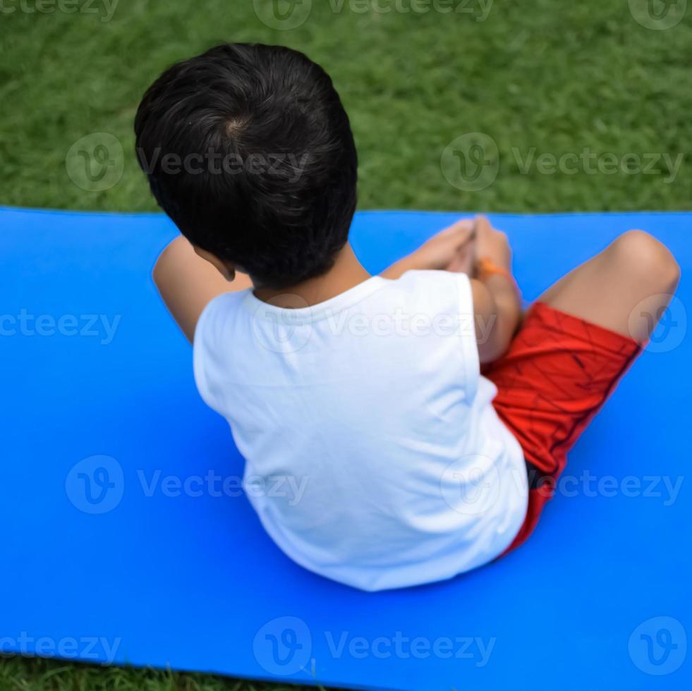 Aziatisch slim kind aan het doen yoga houding in de maatschappij park buitenshuis, kinderen yoga houding. de weinig jongen aan het doen yoga oefening. foto