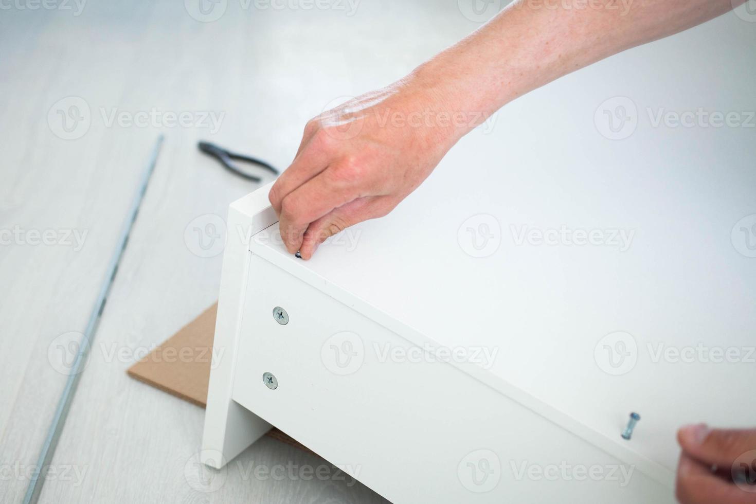 dichtbij omhoog van Mens hand, meubilair assembler maken vlak pak wit meubilair bijeenkomst onderhoud Bij huis. foto