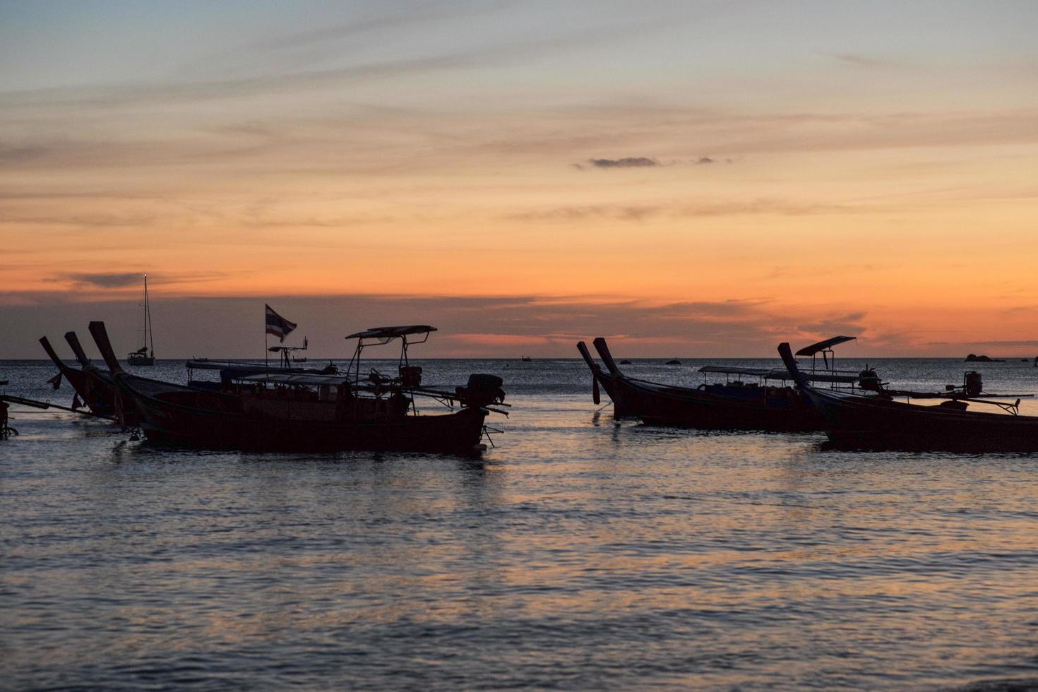 silhouetgroep traditionele lange staartboten die in de zee met schemering van zonsondergang op achtergrond drijven foto