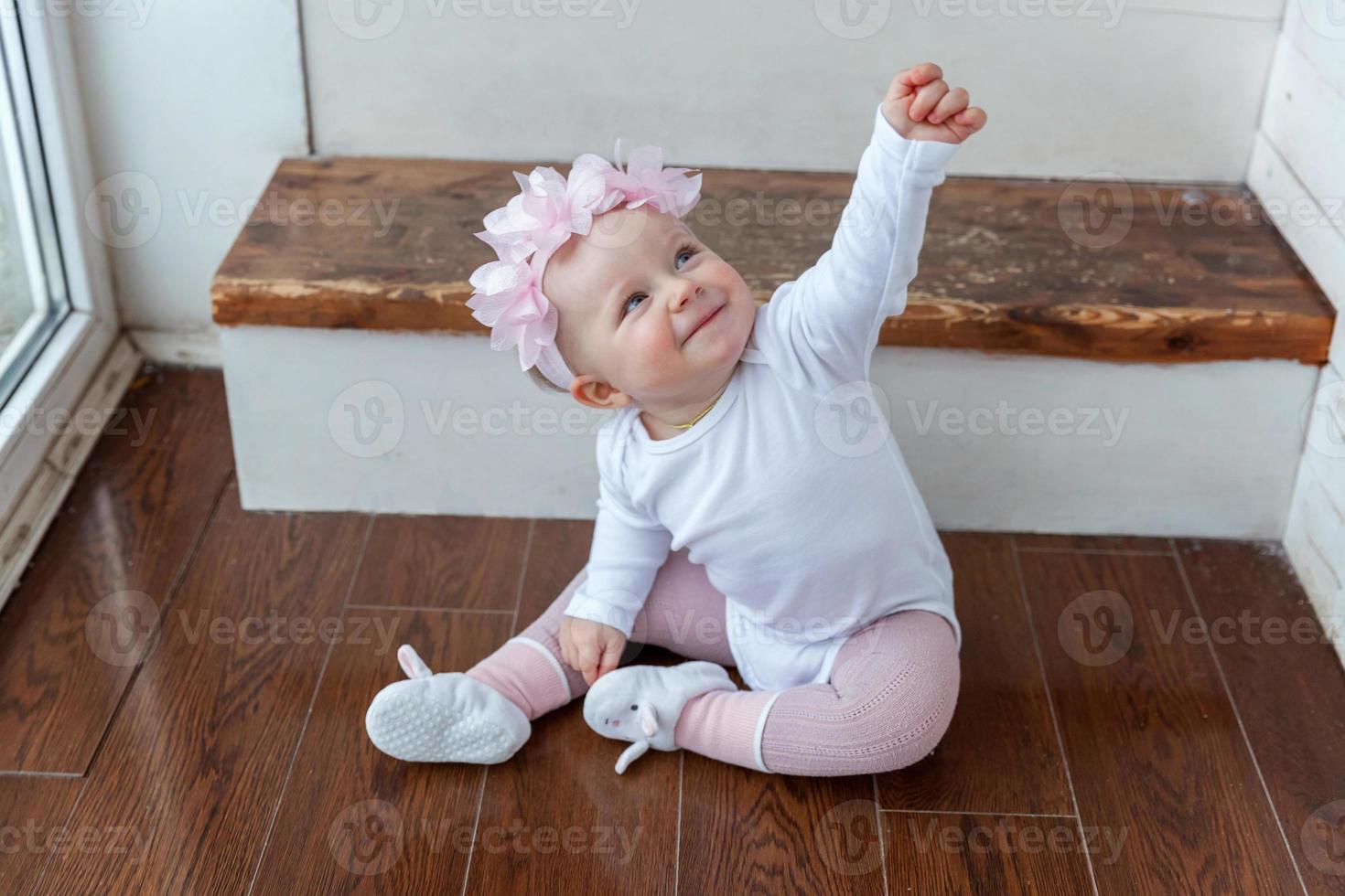 weinig kruipen baby meisje een jaar oud locatie Aan verdieping in helder licht leven kamer in de buurt venster glimlachen en lachend foto