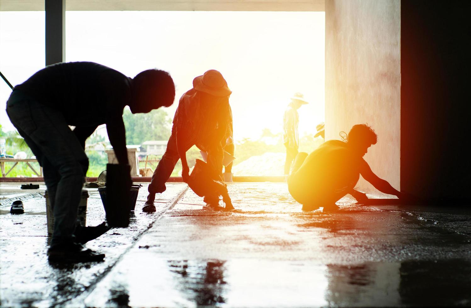 silhouet groep werknemers bouwen de cementvloer in het huis in aanbouw foto