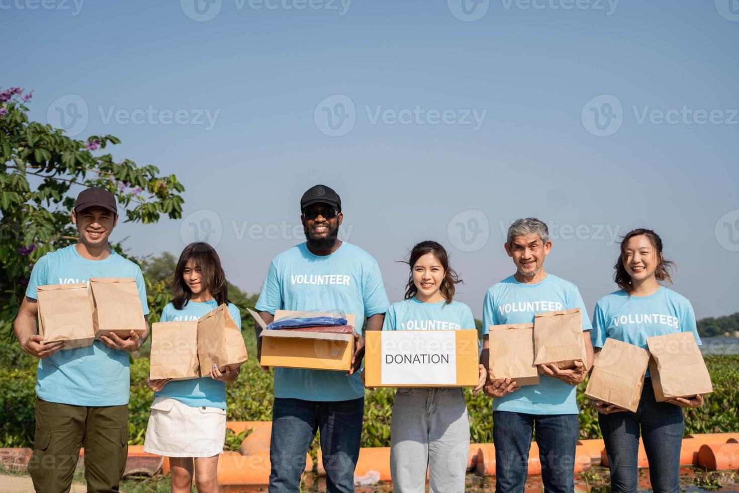 team van vrijwilligers Holding donaties dozen in buitenshuis. vrijwilligers zetten voedsel en overhemd in bijdrage dozen, sociaal arbeider maken aantekeningen liefdadigheid foto