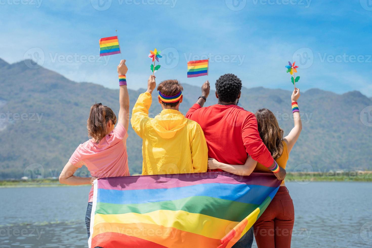 terug visie. jong verscheidenheid mensen Holding homo trots regenboog vlag en kleurrijk turbine Aan de strand. supporters van de lgbt gemeenschap foto