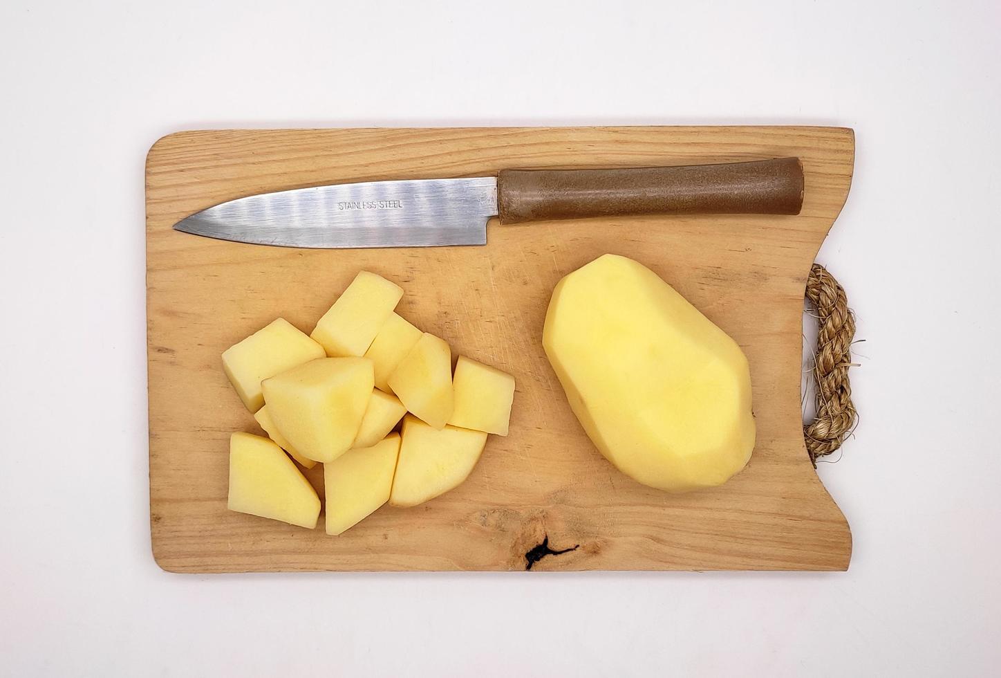 in blokjes gesneden geschild aardappelen en geheel geschild aardappelen, Aan een houten snijdend bord, en een keuken mes. foto