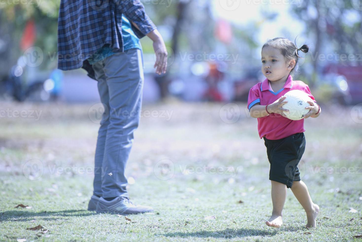 meisje Holding rood voetbal bal in haar handen loopt in park, Toneelstukken met kinderen. kinderen droom in natuur. concept van gelukkig familie kind Speel, gezond levensstijl. foto