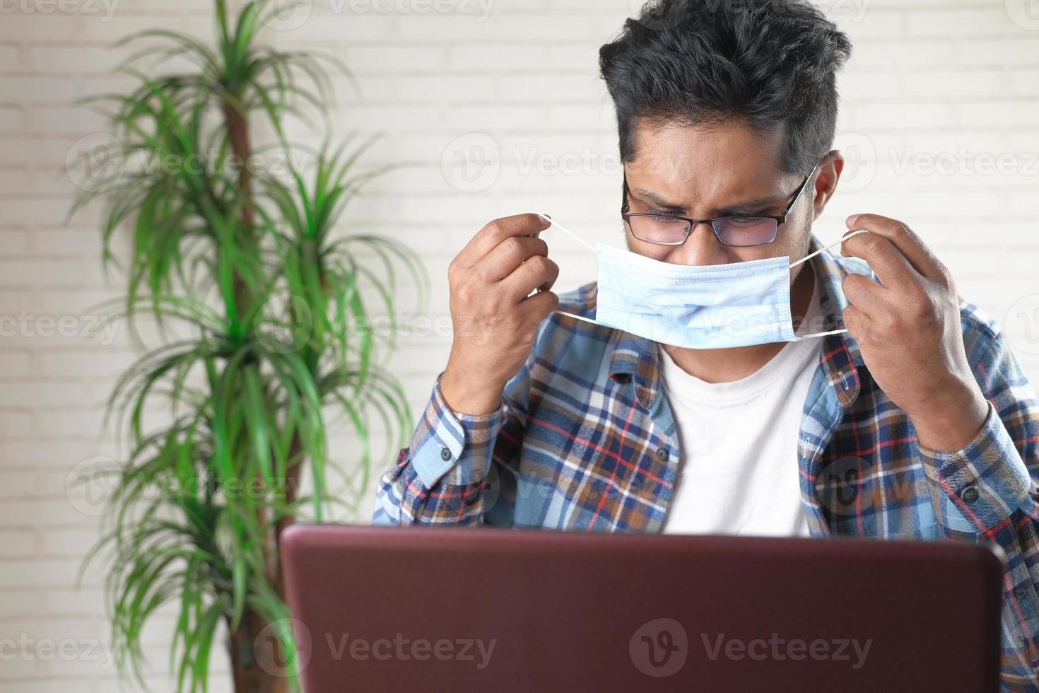 jonge bedrijfspersoon die beschermend masker draagt tijdens het werken op laptop foto