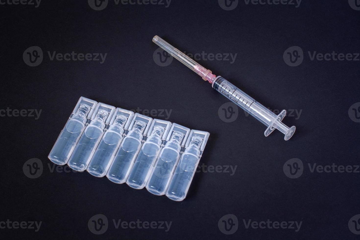 ampullen met een vaccin en een injectiespuit liggen Aan een donker achtergrond. beschikbaar injectiespuit voor persoonlijk gebruiken. vignettering. horizontaal. foto