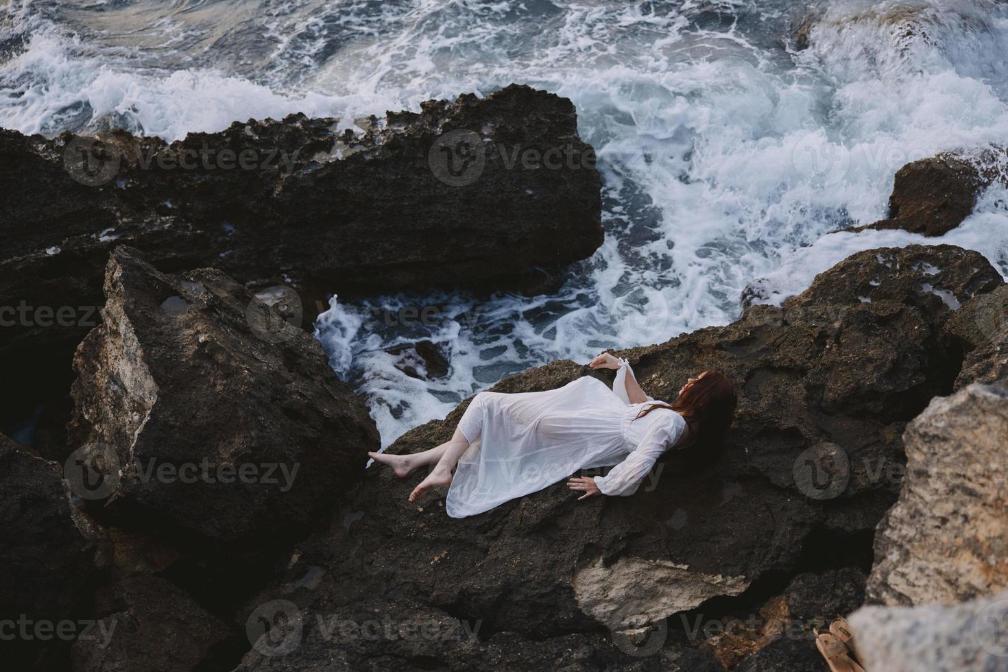 sensueel vrouw in een afgelegen plek Aan een wild rotsachtig kust in een wit jurk landschap foto