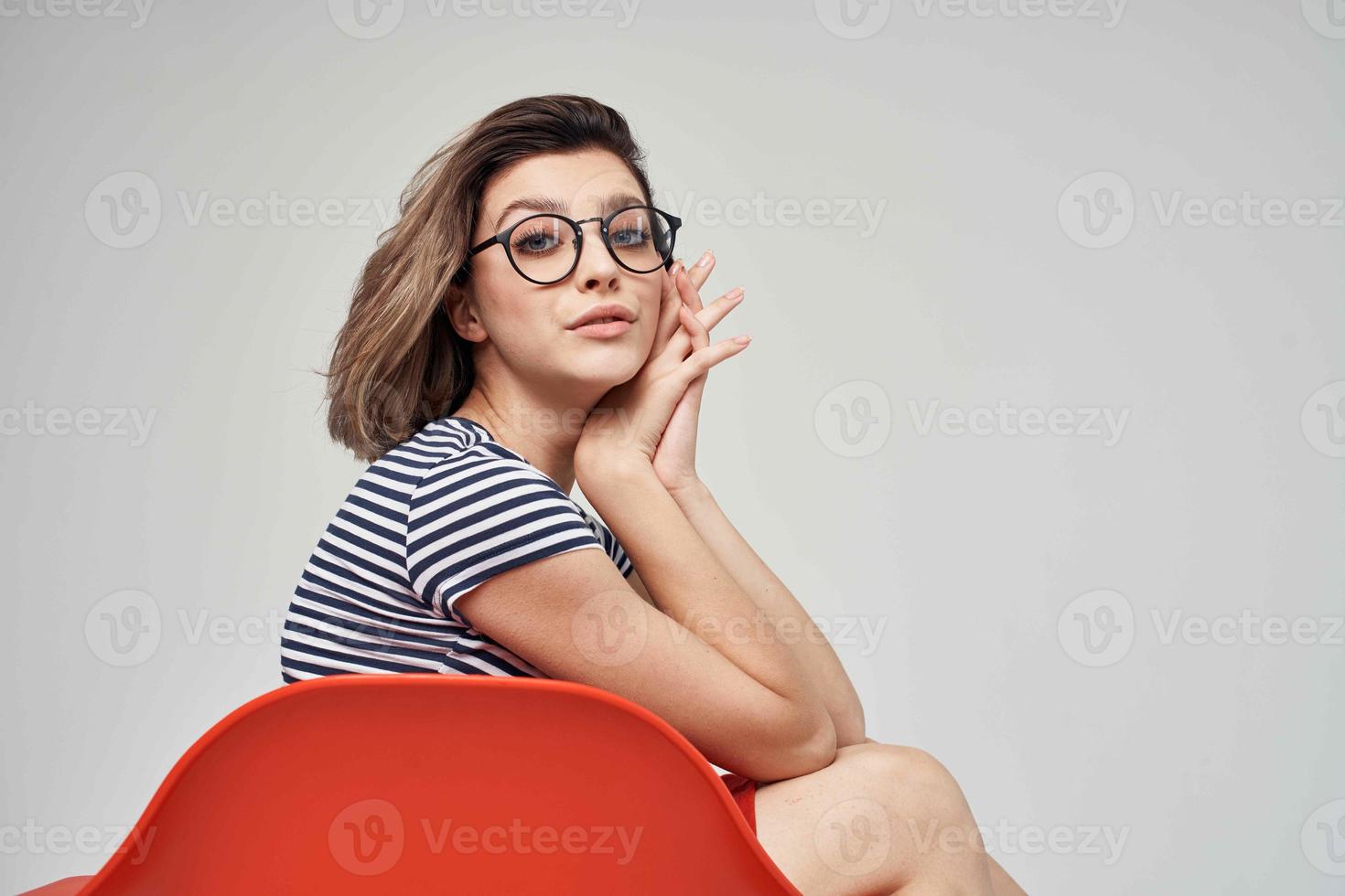 vrouw met bril zittend Aan de rood stoel licht achtergrond levensstijl foto