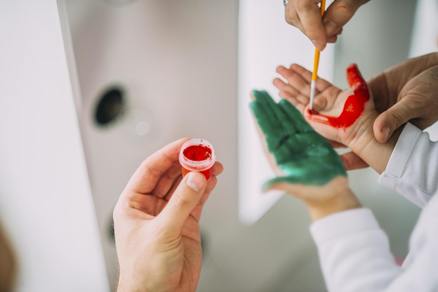 ouders verf aanbrengen op de handen van het kind foto