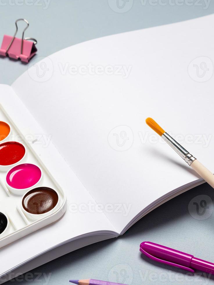 Open blanco vel van schetsboek met aquarellen, gouache, borstels en andere schrijfbehoeften Aan een licht achtergrond, kopiëren ruimte foto