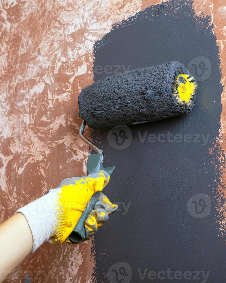 handgeschilderde huismuur met grijze acrylverf met een roller in gele werkhandschoenen foto