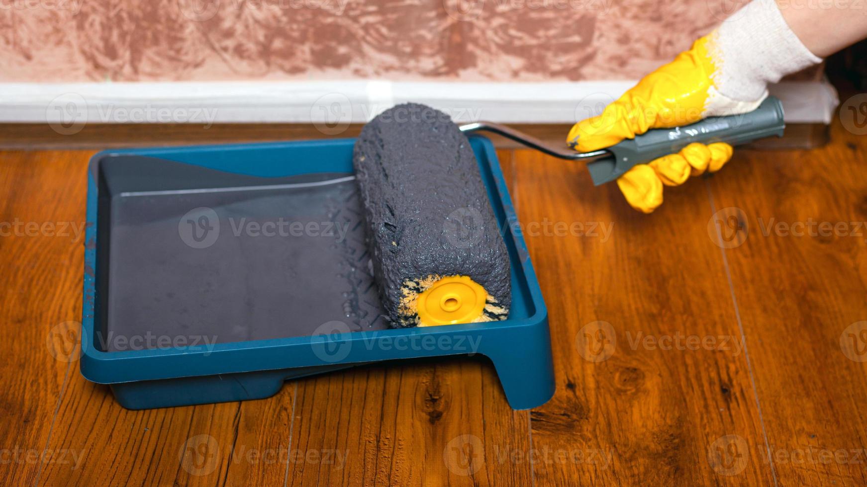 hand in gele handschoen dips roller in een bakje met grijze verf voor het schilderen van muren foto