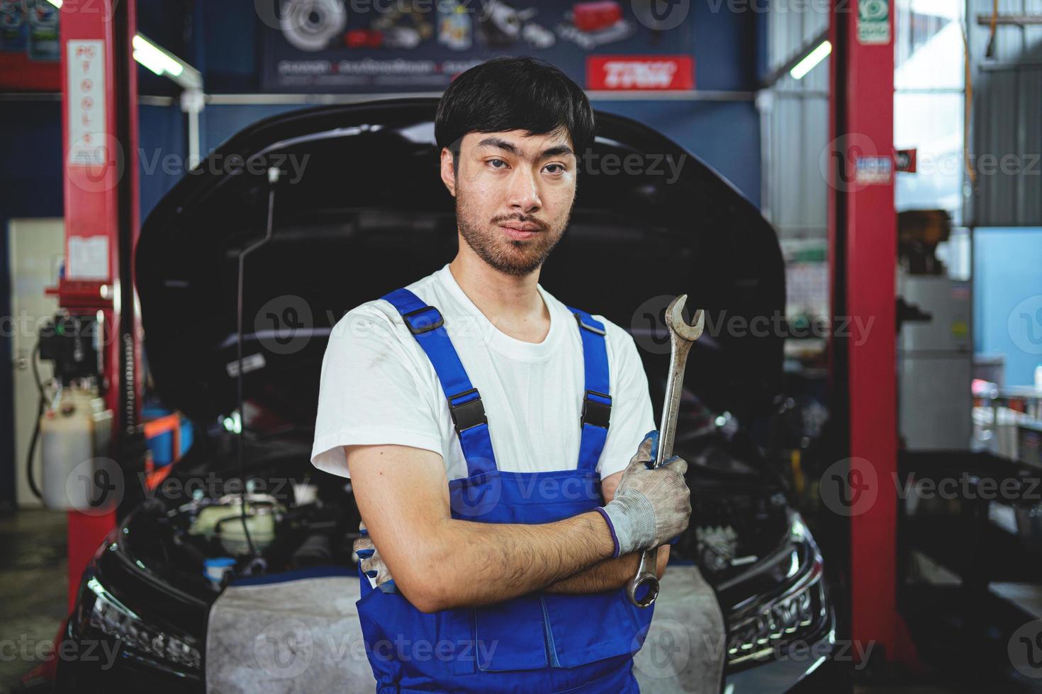 portret van een zelfverzekerd Aziatisch mannetje monteur Bij een garage. motor onderhoud onderhoud controle de staat van de auto. reparatie onderhoud concept. foto