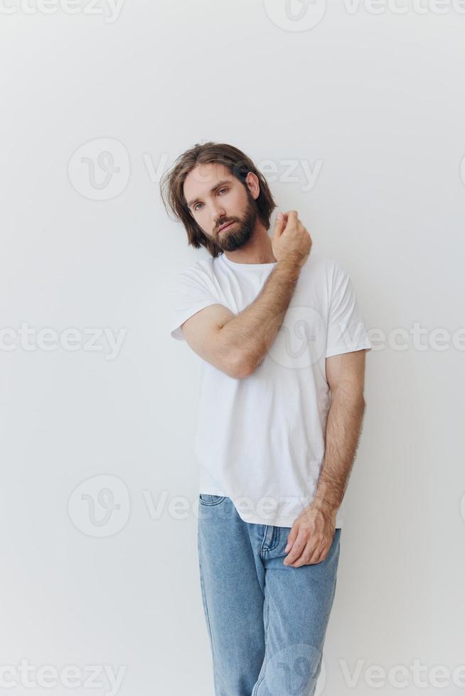 een Mens in een wit t-shirt en blauw jeans staat tegen een wit muur en poses foto