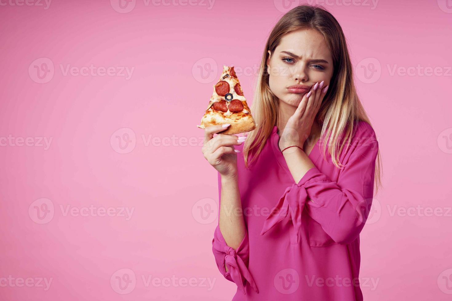 vrolijk blond met pizza in haar handen rommel voedsel tussendoortje roze achtergrond foto