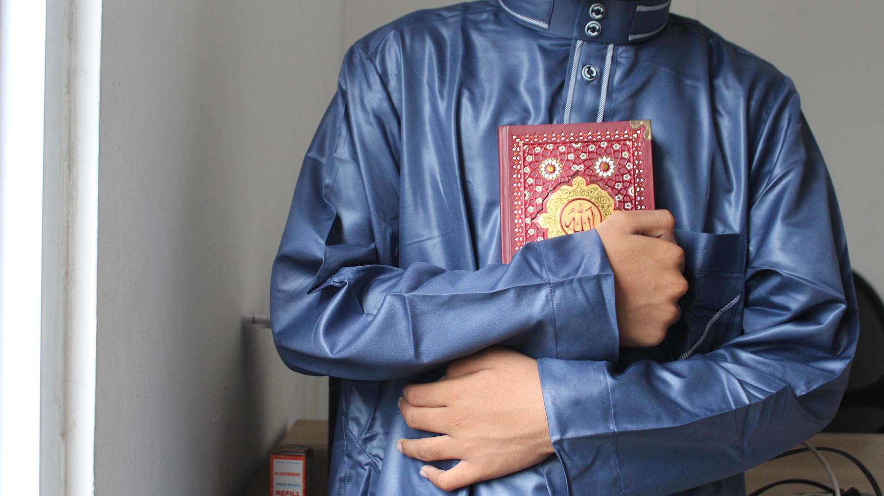 een jong moslim Mens is Holding de Koran naar zijn borst. foto