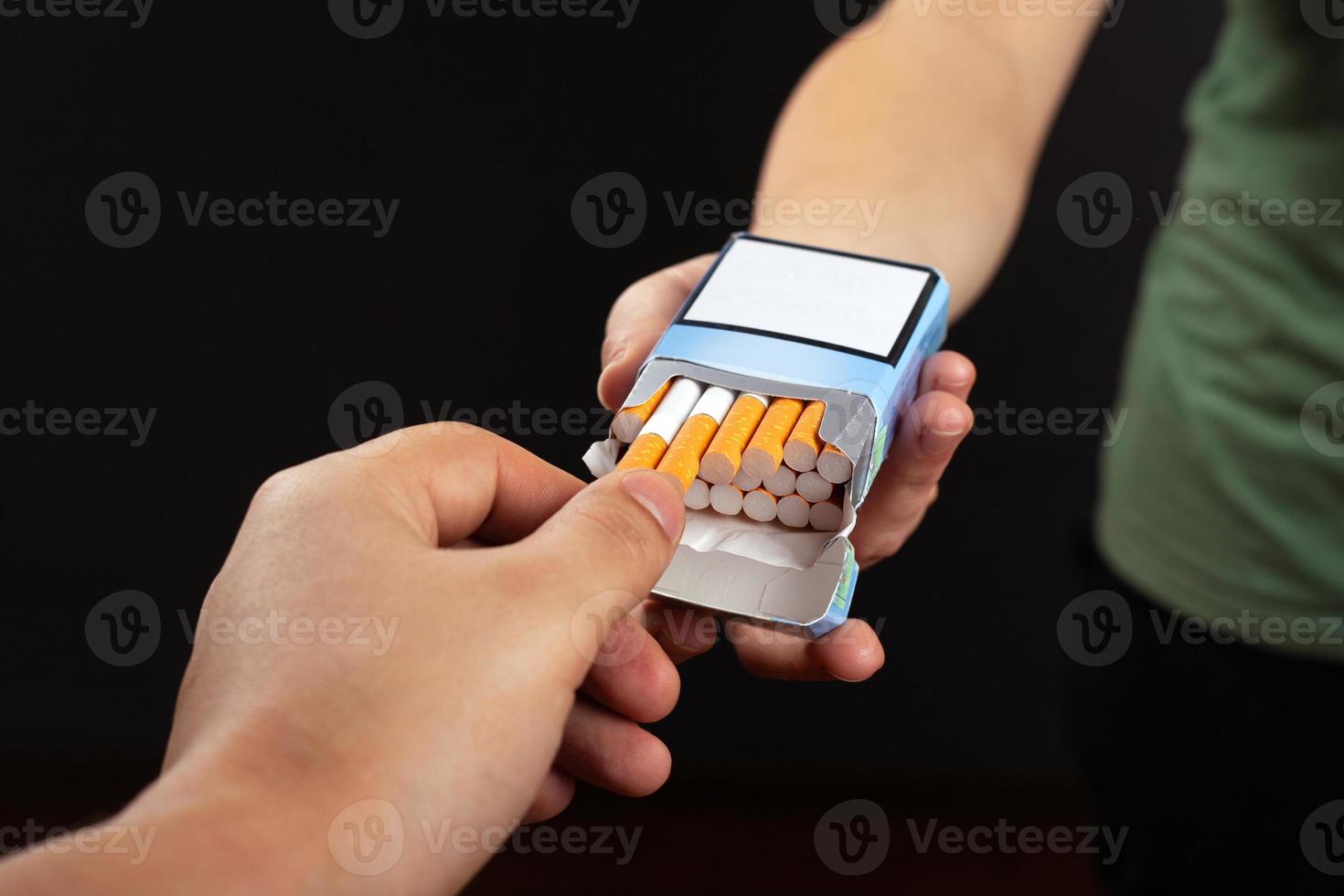 hand neemt een sigaret uit een pak op een donkere achtergrond foto
