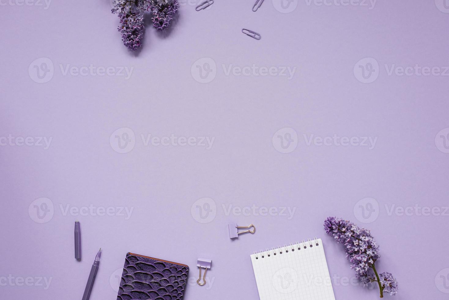 kladblok en pen, papier clips en clips met een lay-out van de plaats naar kopiëren. huis kantoor bureaublad met top visie, versierd met lila bloemen foto