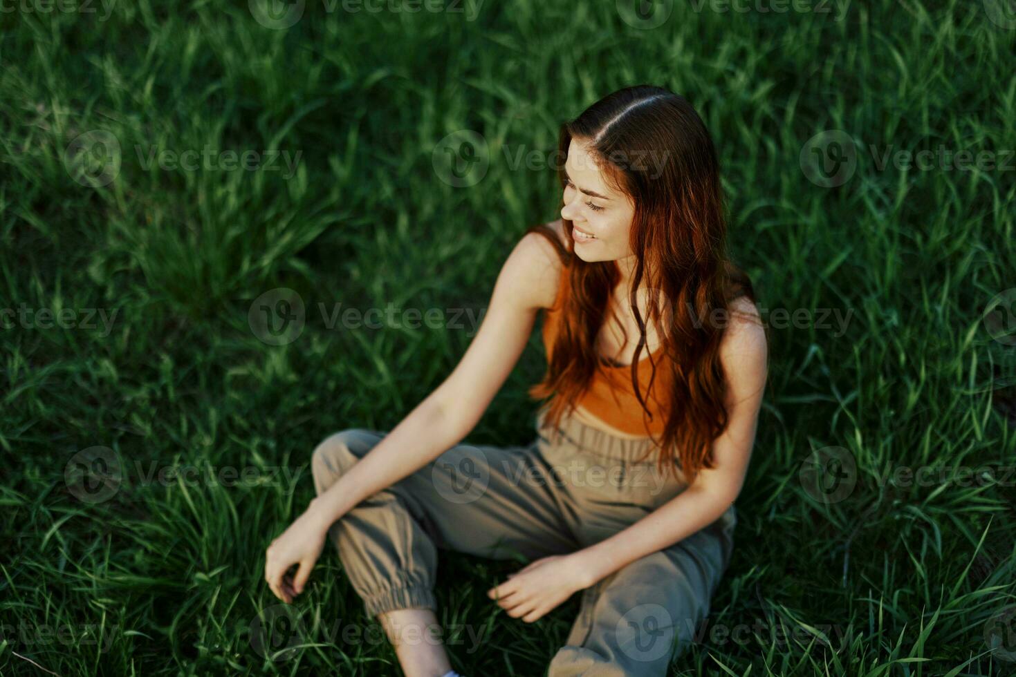 freelance vrouw zittend in een park in zomer Aan de gras op zoek Bij de zonsondergang, zonneschijn in natuur foto