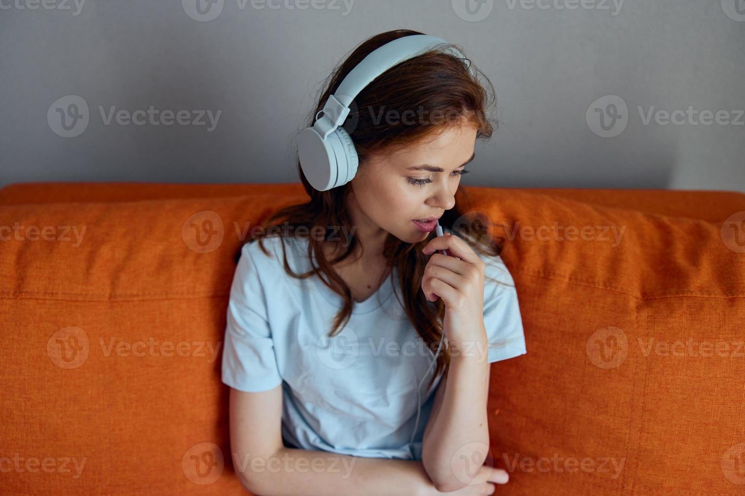 vrolijk vrouw zittend Aan de bankstel Bij huis luisteren naar muziek- Aan hoofdtelefoons appartementen foto