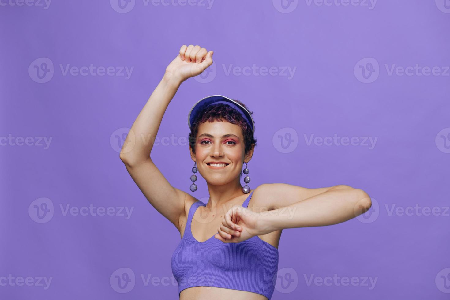 sport- mode vrouw dansen poseren glimlachen met tanden in een Purper sport- pak voor yoga Aan een slank lichaam en een transparant pet Aan haar hoofd Aan een Purper achtergrond monochroom foto