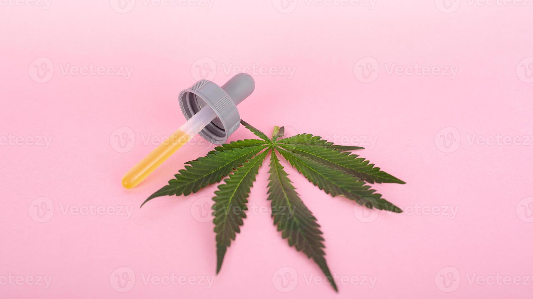 cannabisblad en pipet met psychoactief thc-concentraat-extract op roze achtergrond foto